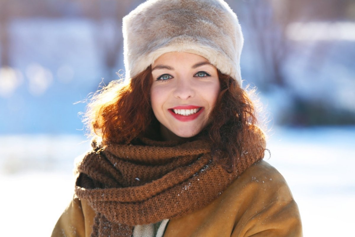 Smiling woman in a fur hat and knit scarf on a sunny snowy day