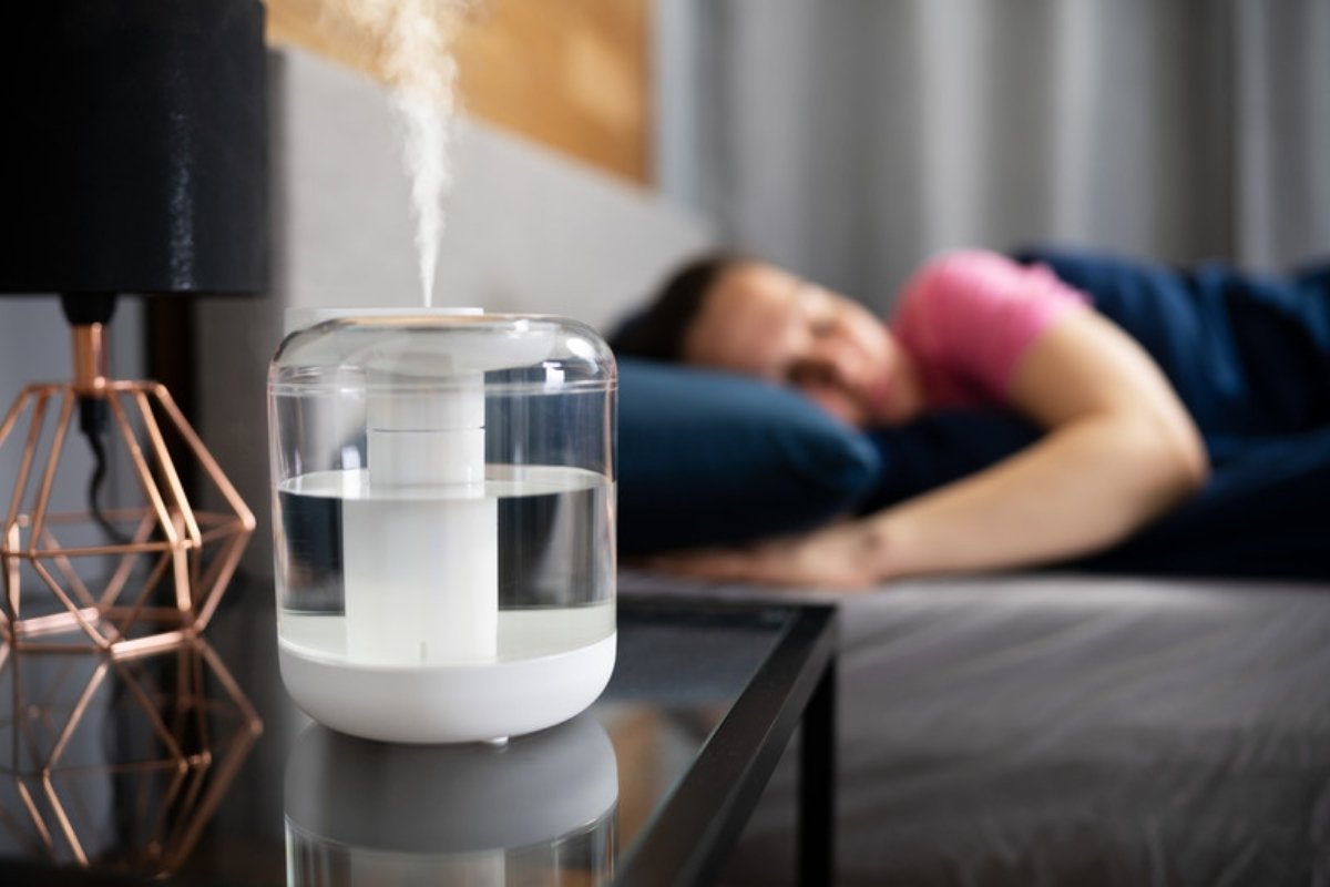 Humidifier releasing mist on a bedside table while a woman sleeps